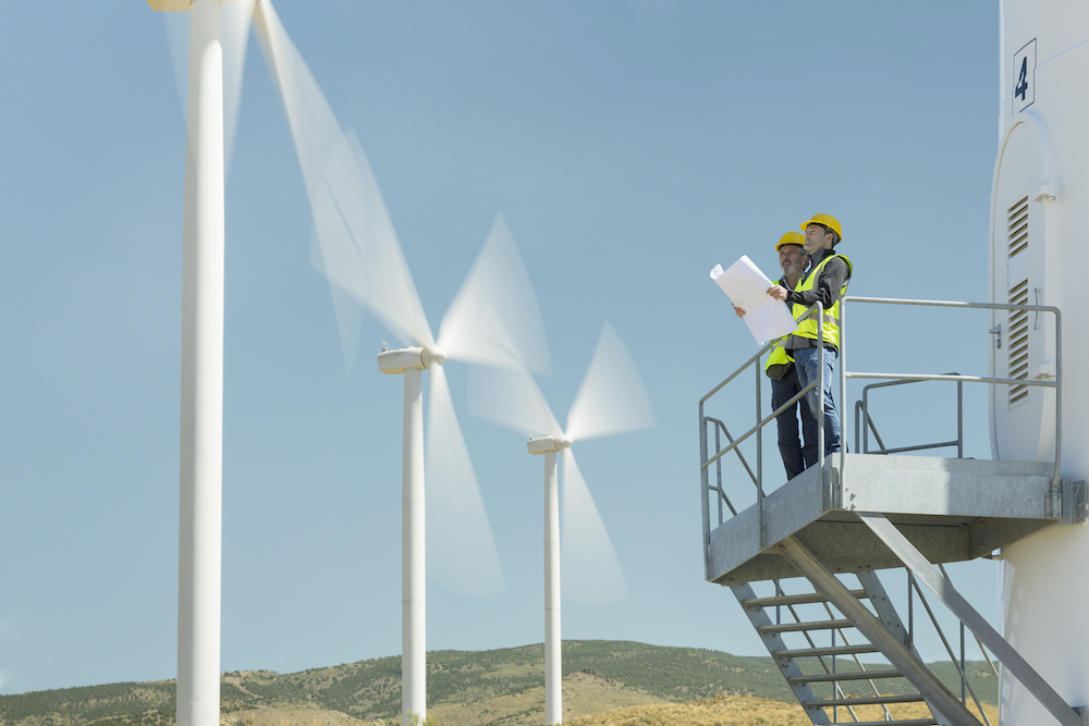 Workers standing on wind turbine in rural landscape