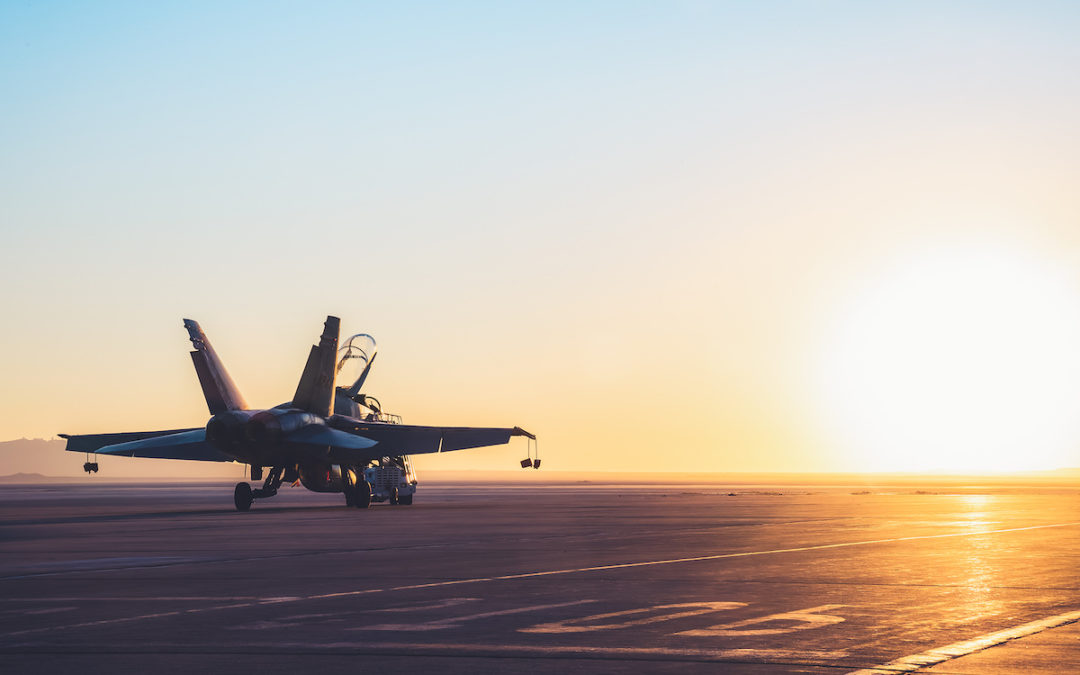 Jet fighter on an aircraft carrier deck against beautiful sunset sky.