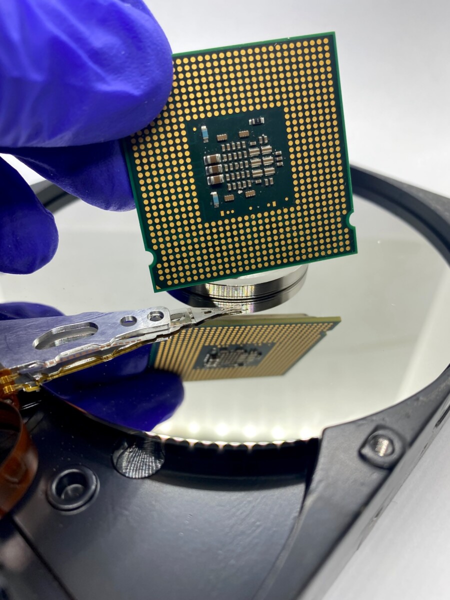 A blue-gloved hand holds a microchip over a reflective plate.